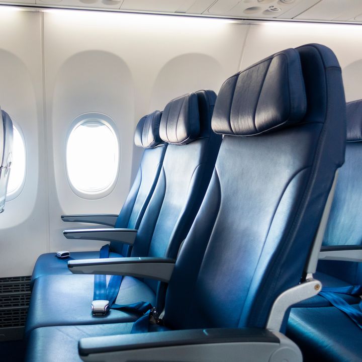 Rows of empty blue airplane seats facing the window.