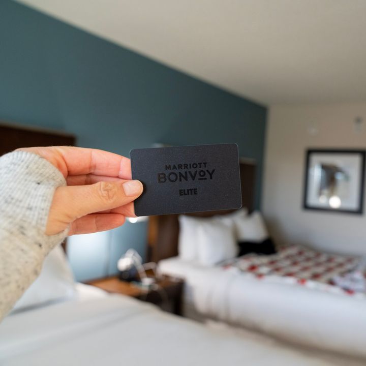 A hand holding a black Marriott Bonvoy card inside a hotel room.