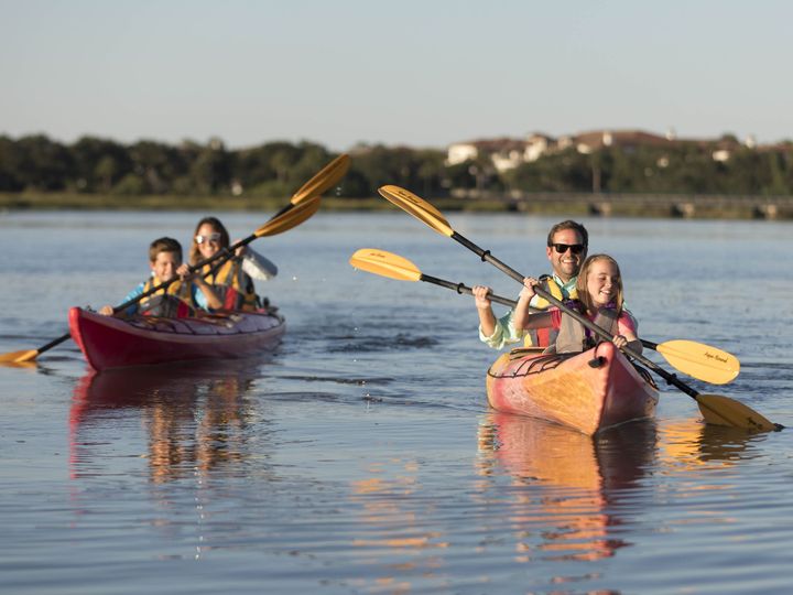A family of four kayaks in two separate kayaks while smiling.