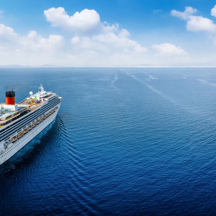An aerial view over a cruise ship that is seen sailing along an empty blue sea.