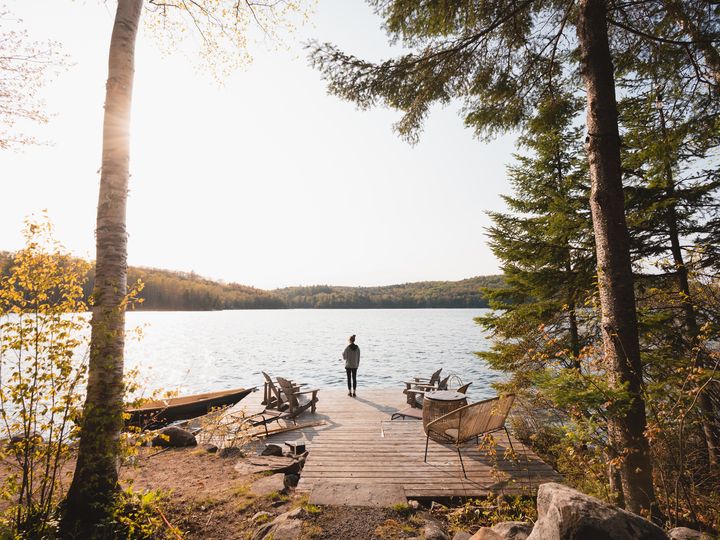 A person stands out on a dock jutting into the lake in Muskoka. The sun is rising, and trees surround the area.