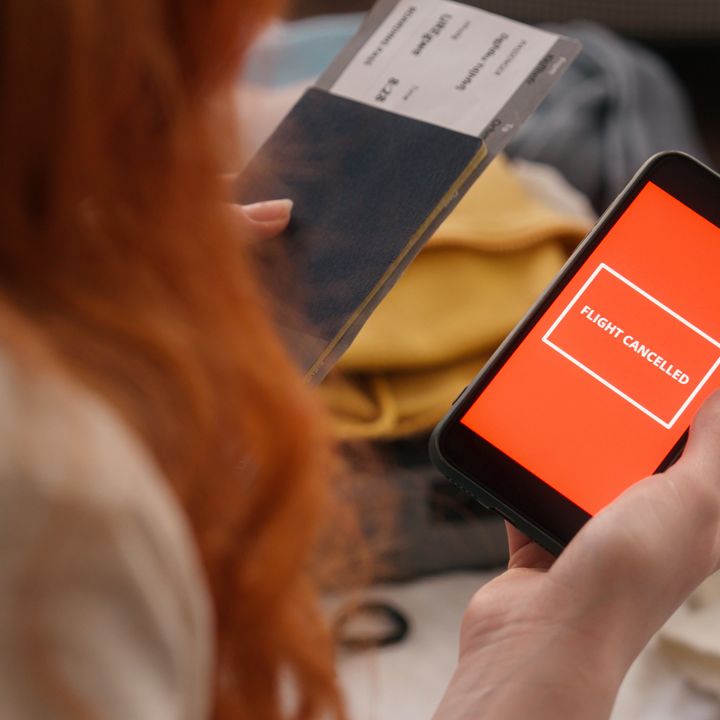 A woman whose face is not visible is seen holding a passport and a phone that says ‘flight canceled’ on the screen.