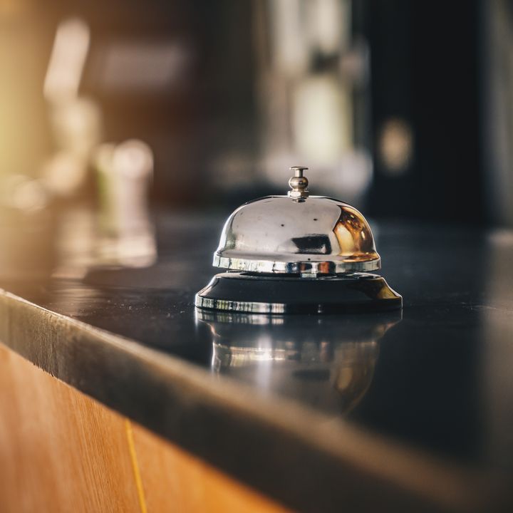 A bell sits on a black hotel desk reception counter with nothing else around it.
