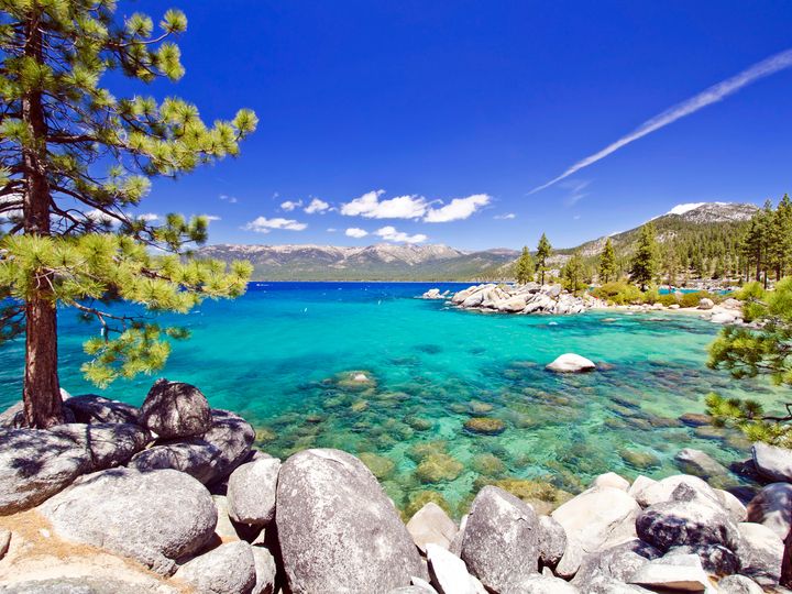 A shoreline along Lake Tahoe with clear bright blue water and a rocky water’s edge.