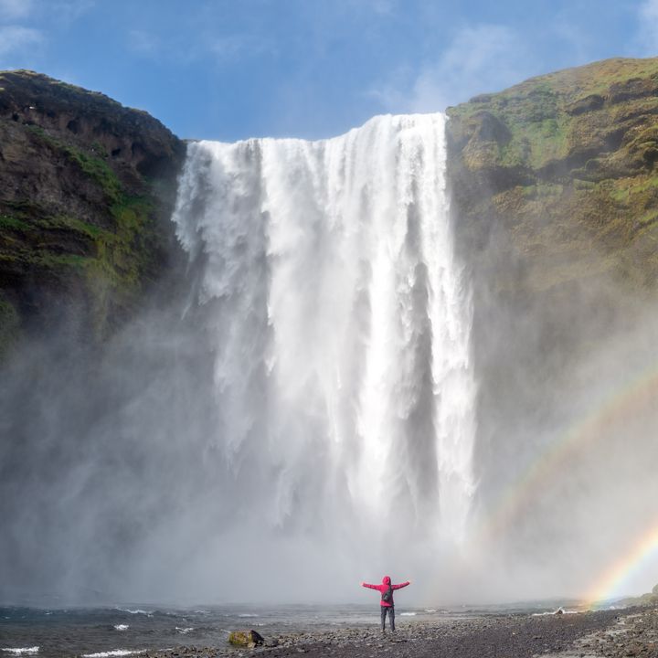 Person standing at foot of cascading waterfall with double rainbow