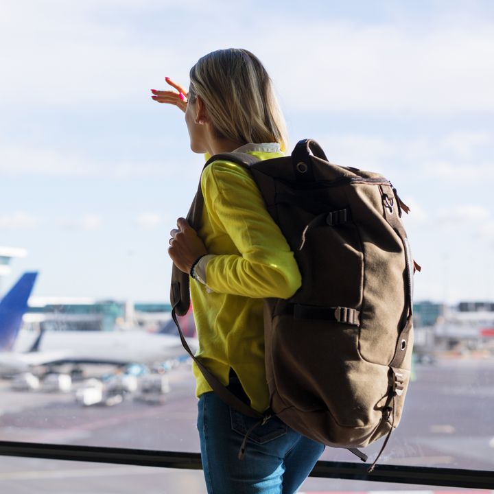 Woman in airport wearing large backpack and watching planes take off from the terminal