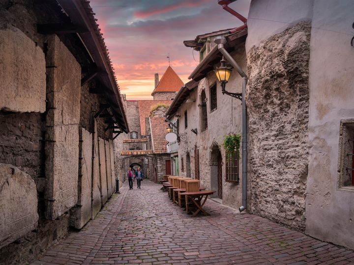 A narrow historic street in Old Town Tallinn, Estonia, with stone walls and cobblestone street.