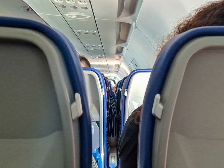 An eye-level view of rows of airplane seats filled with people.