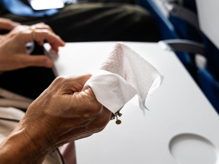 A hand is seen holding a cleaning wipe to clean a tray table on a plane.