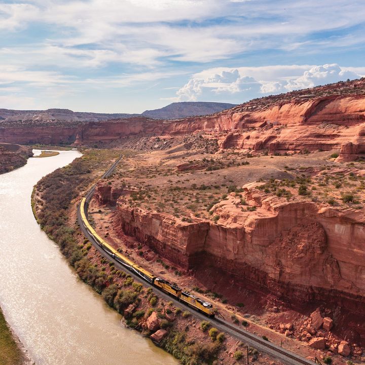 A Canyon Spirit train next to a river and Utah's red rock formations.
