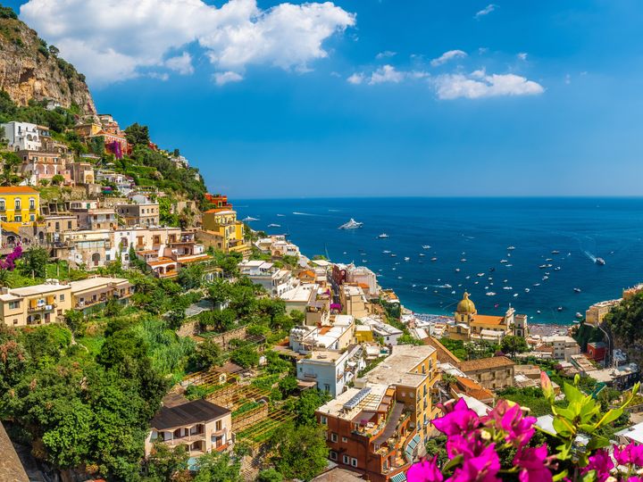 Hillsides dotted with buildings and trees and flowers with views of the water along the Amalfi Coast.