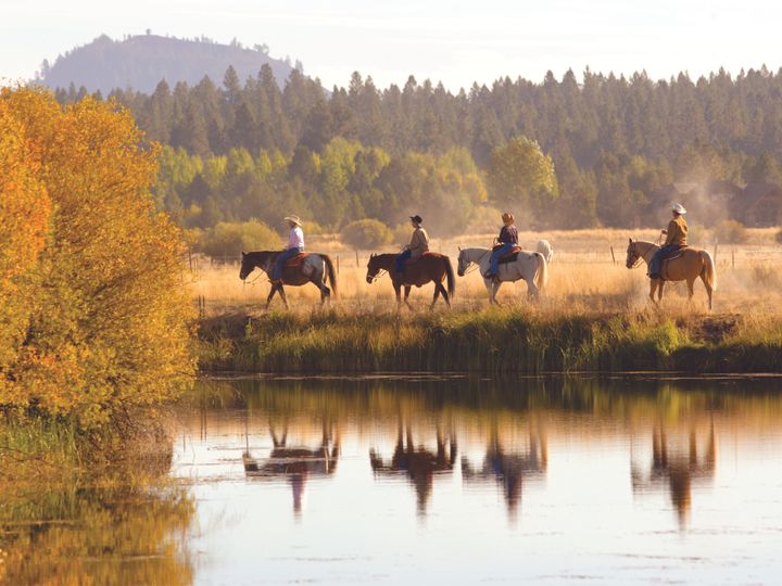 A group of horseback riders next to a river and fall foliage at Sunriver Resort in Oregon. 
