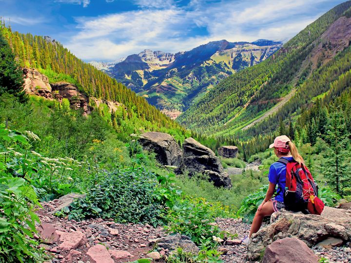 A hiker rests on a rock at the top of the Bear Creek Trail in Telluride, Colorado, during summer.