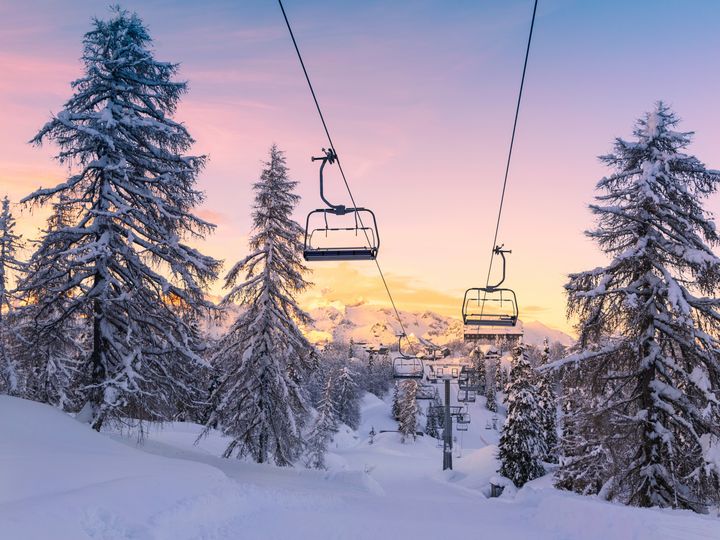 A chairlift is visible over a snowy mountain at sunset in winter.