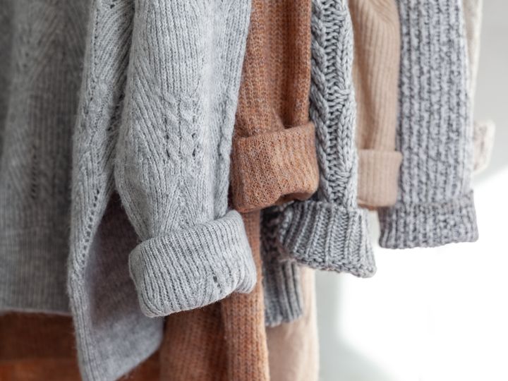 Several wool sweaters are hanging with their sleeves in a row, all in neutral colors.