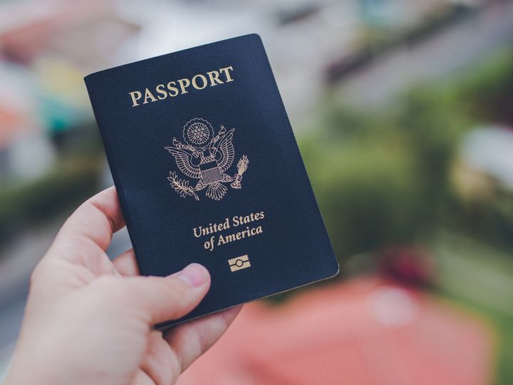 A hand holding out a US passport against a blurred background.