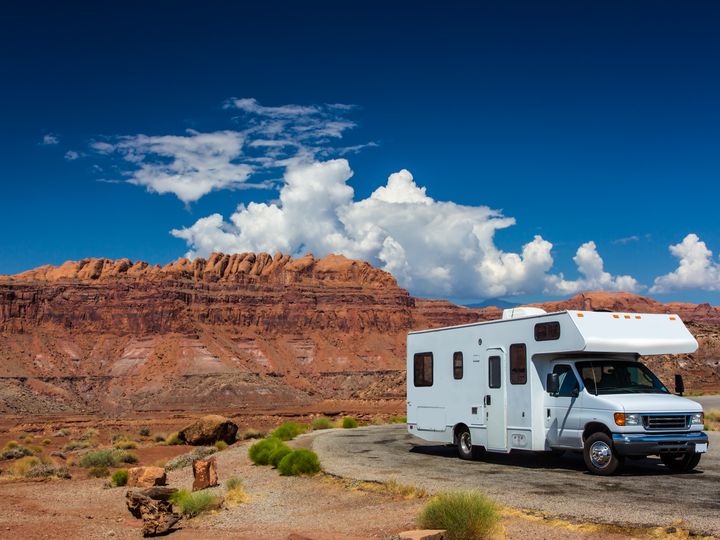 A white RV is seen parked in Canyonlands National Park, Utah, next to red rock formations.