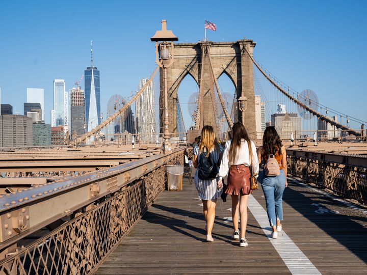 Teenagers walk over the Brooklyn Bridge as seen from behind.