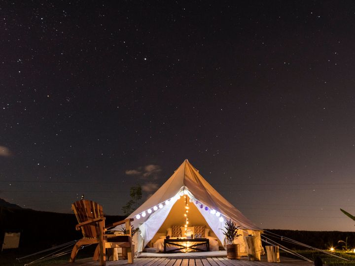 A glamping tent on a deck with an Adirondack chair under a starry night sky.