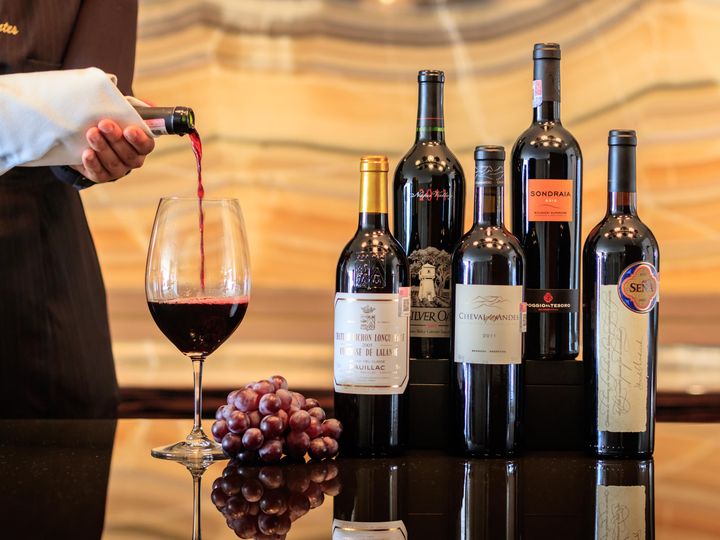A hand is seen pouring a glass of wine next to a group of bottles. 