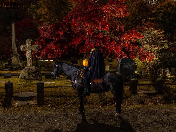 A black horse with what looks like a headless rider on top in the Sleepy Hollow Cemetery at night in fall.