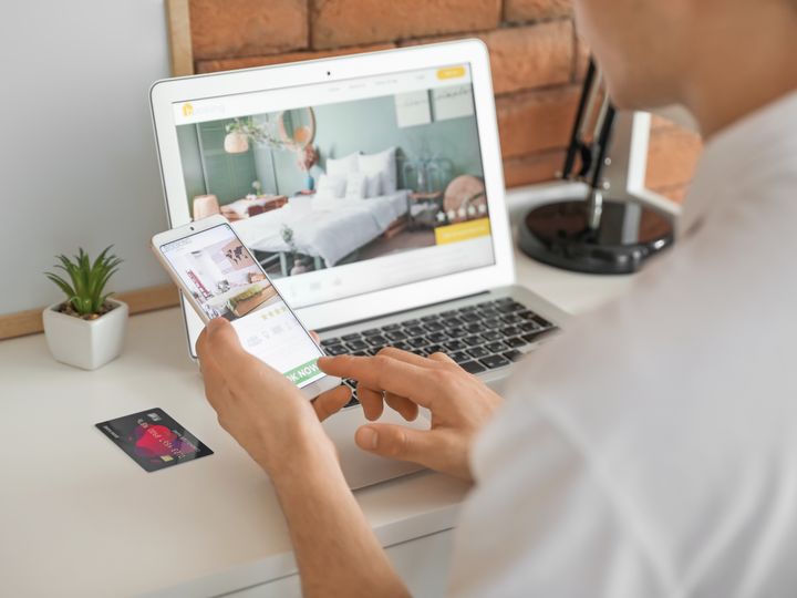 A person is seen booking a hotel room on a laptop while holding a mobile next to a credit card.