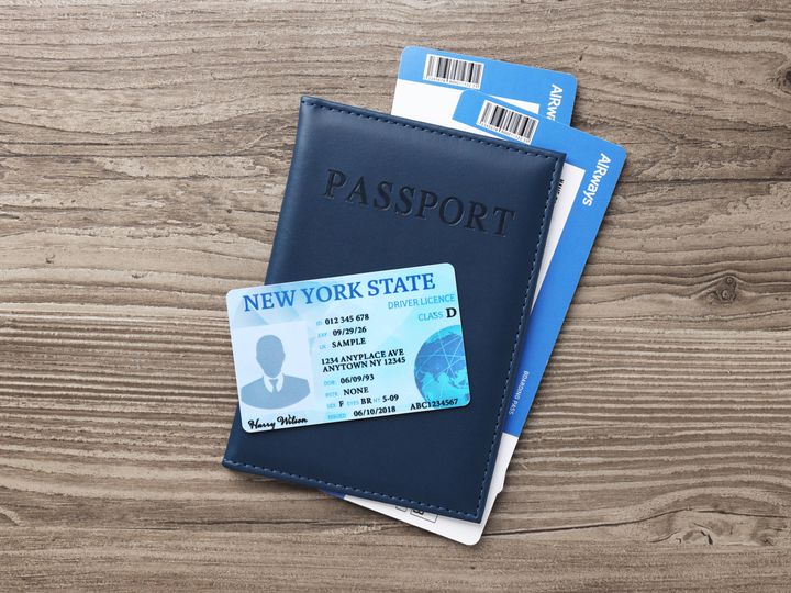 A card that says it’s a New York State ID is placed on top of a passport case that contains what appear to be two plane tickets.