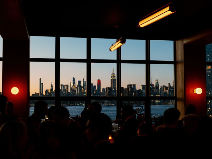 A bar with a large window overlooking the Manhattan skyline at dusk