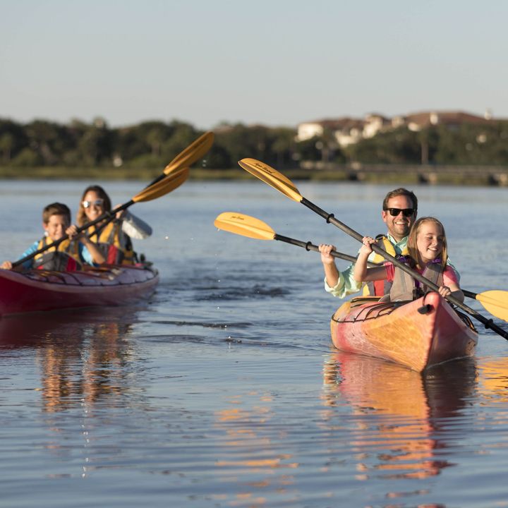 A family of four kayaks in two separate kayaks while smiling.