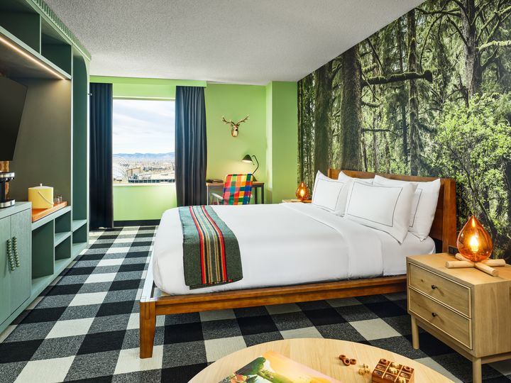 A camping themed room at The Curtis Hotel with woodsy wallpaper, a fireplace-style lamp, taxidermy, and other accents.