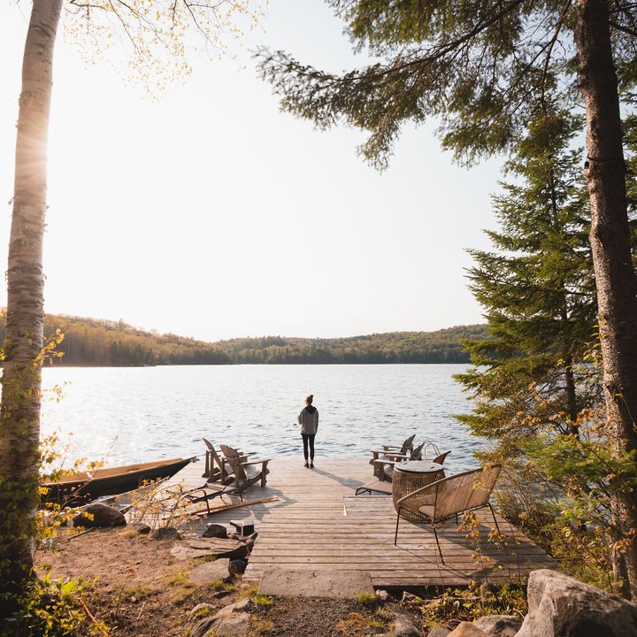 A person stands out on a dock jutting into the lake in Muskoka. The sun is rising, and trees surround the area.