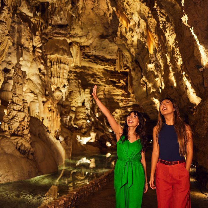 Two women walk inside a cavern and are seen admiring their surroundings.