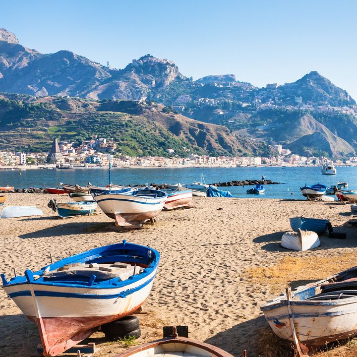 Several boats sit on the sand in Naxos with the sea and mountains behind them.