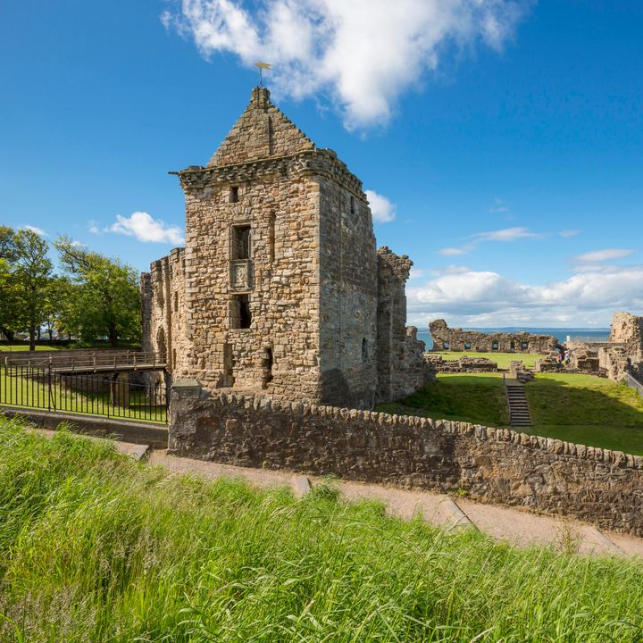 The ruins of St. Andrews Castle in Scotland next to the sea under a blue sky.