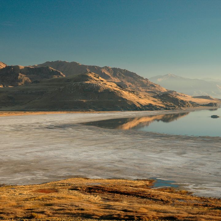 The dramatic landscapes of Antelope Island inside Great Salt Lake with large mountains and a sparse shore all lit gold by the sun.