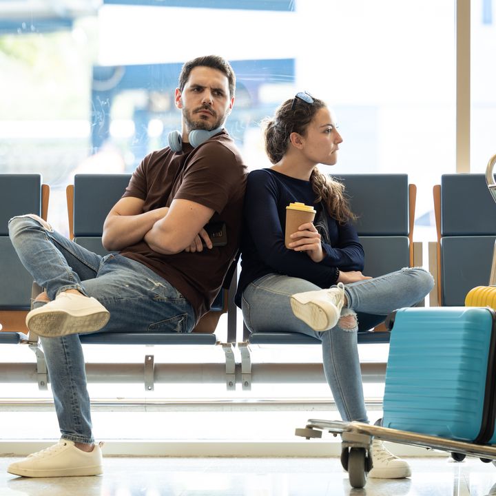 Couple fights at the airport while waiting for their plane. Couple turn their backs on each other angry.