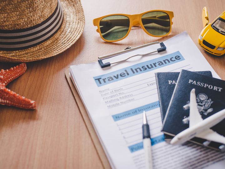 A clipboard with travel insurance paperwork plus passports, a pen, sunglasses, a hat, starfish, and toy plane and car.