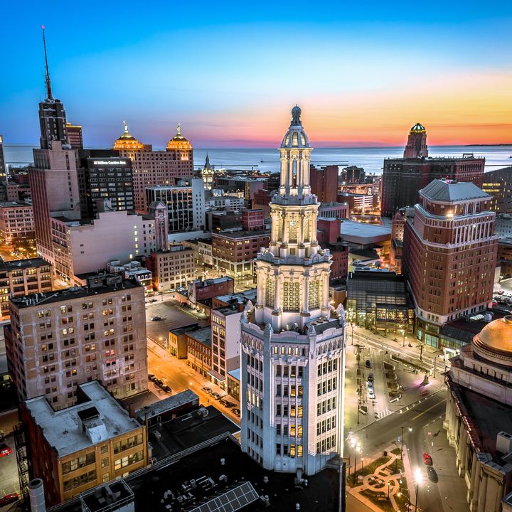 A skyline view of downtown Buffalo, New York, at sunset with pink and orange skies in the background and the Electric Tower skyscraper in the foreground.