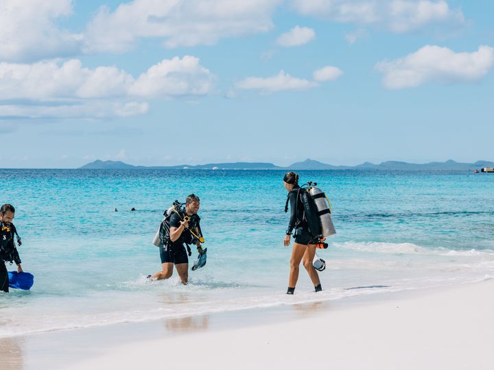 Three scuba divers emerging from the blue waters on a tropical beach in Bonaire.