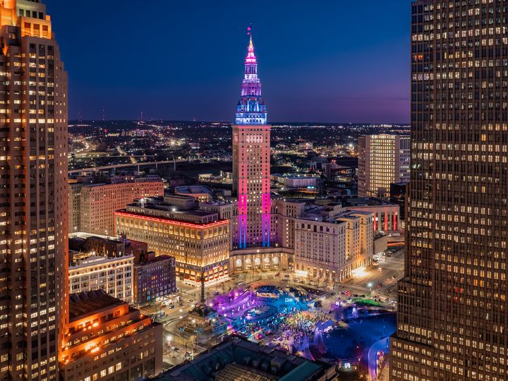 Buildings in Cleveland lit up at night, including a central skyscraper with colorful neon lights.