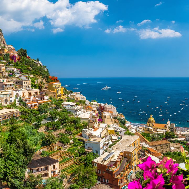 Hillsides dotted with buildings and trees and flowers with views of the water along the Amalfi Coast.