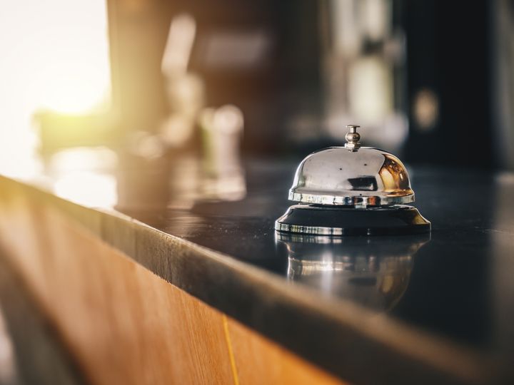 A bell sits on a black hotel desk reception counter with nothing else around it.