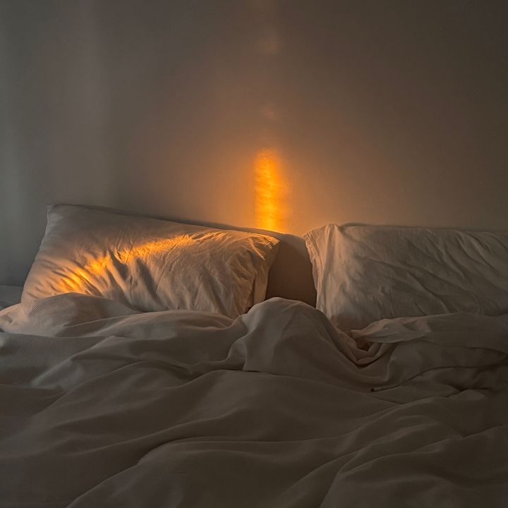 A bed with two white pillows and a white duvet with a sliver of golden sunlight spilling in.