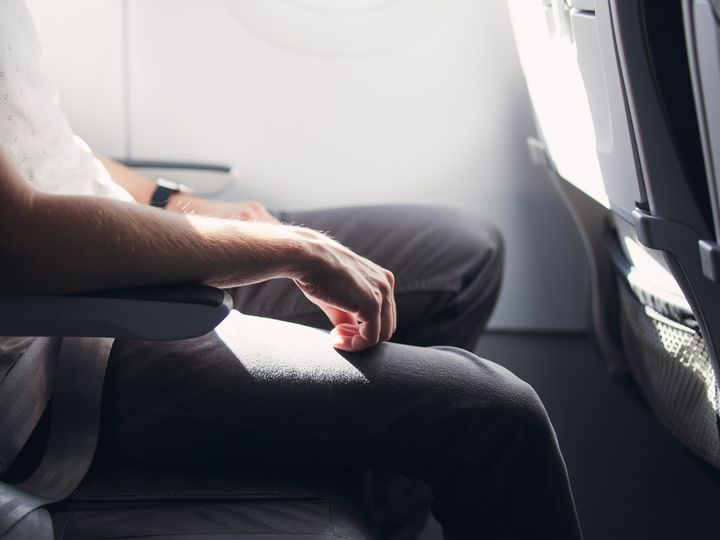 A man’s lower half is seen sitting on an airplane with lots of extra legroom.