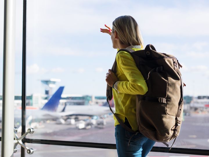 Woman in airport wearing large backpack and watching planes take off from the terminal