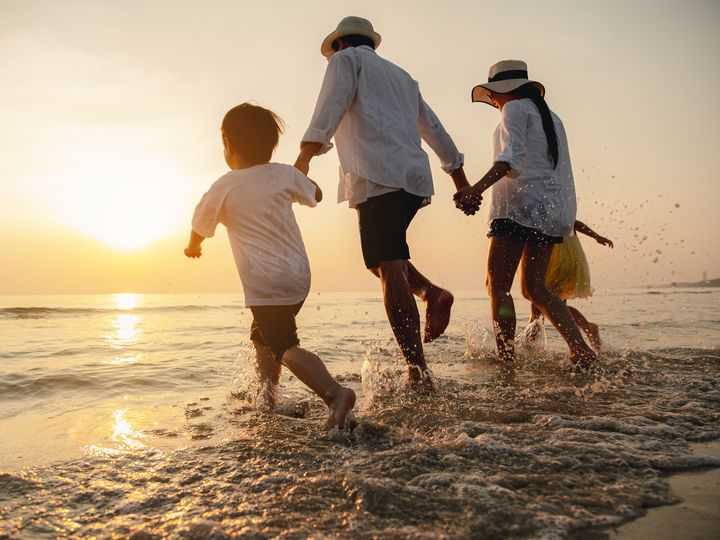 A family holding hands and running toward the beach at sunset.