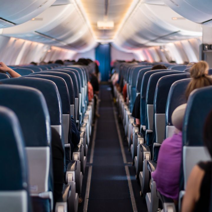  A view from the back of a plane looking forward through the aisle with rows of plane seats filled with passengers.