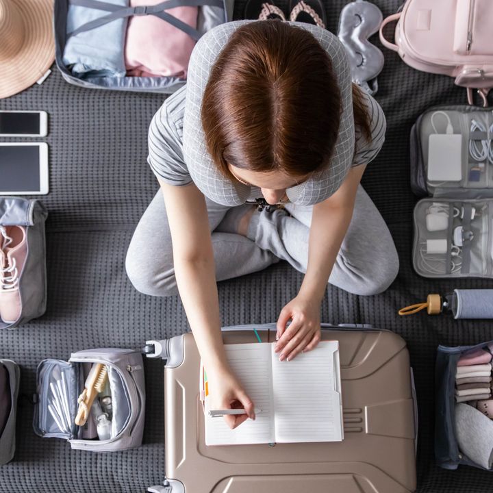 An overhead shot of a woman packing, surrounded by packing cubes and accessories of various sizes as she writes on a notebook on top of her suitcase.