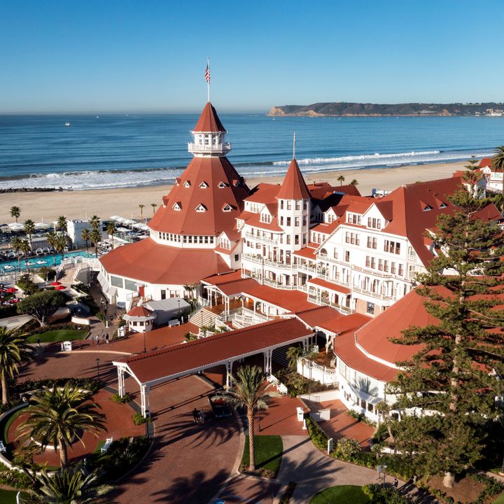 An aerial view of the red roofed Hotel del Coronado showcasing its beachfront location and entrance.