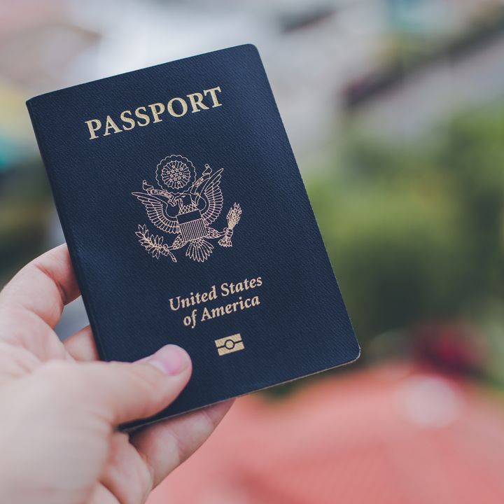 A hand holding out a US passport against a blurred background.